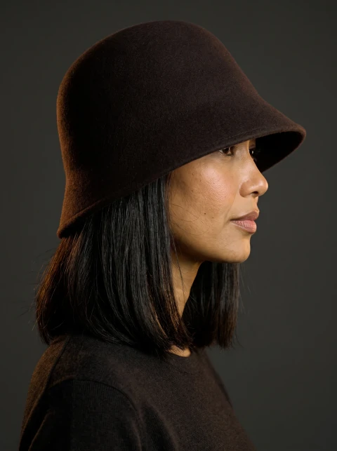 Profile portrait of a woman wearing a dark brown felt bucket hat with a low brim.