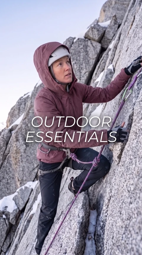 Climber in a plum hooded jacket, helmet and gloves, secured by a rope. “OUTDOOR ESSENTIALS”.